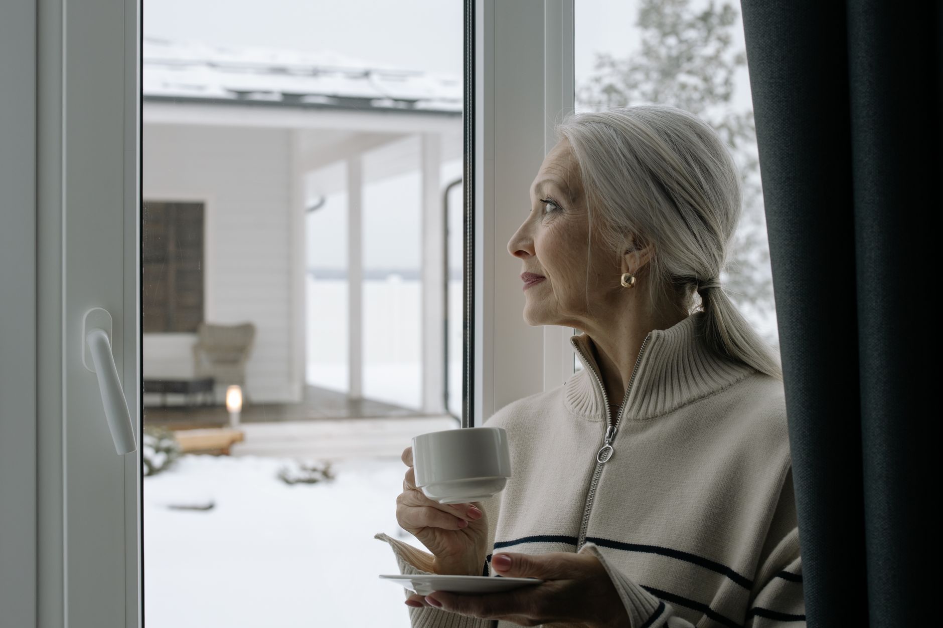 Older woman holding a coffee cup and looking out a window